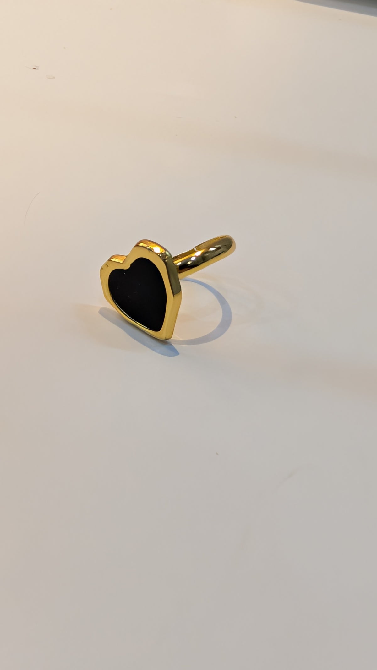 Gold-tone ring with a black heart-shaped inlay on a plain white background