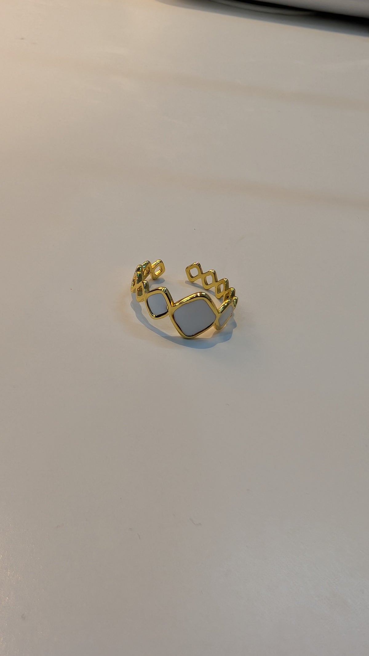 Gold-tone ring with a central rectangular cutout and small circular openings along the band.