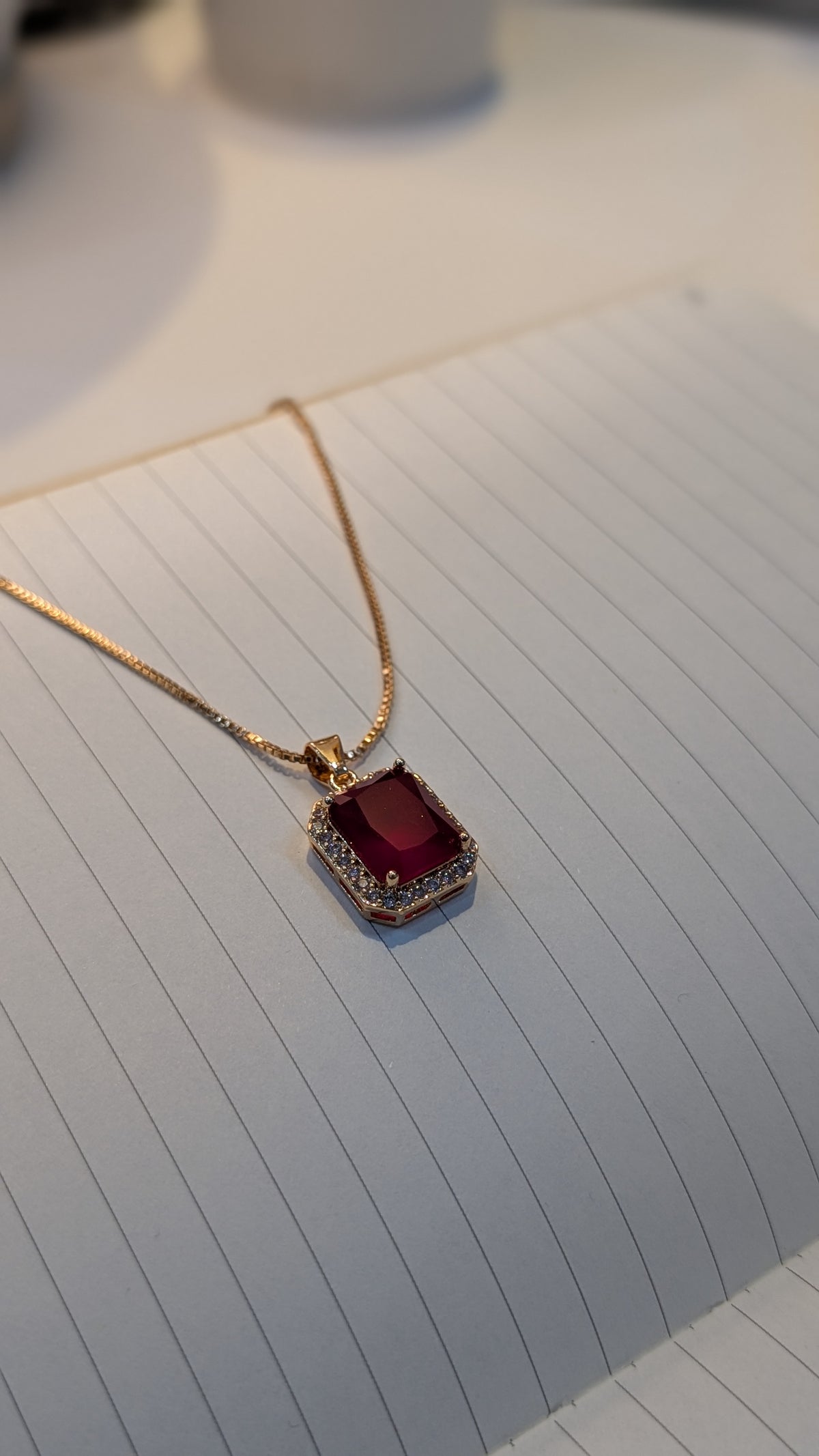 Gold-tone necklace with a rectangular pendant containing a deep red center surrounded by small clear/white stones.