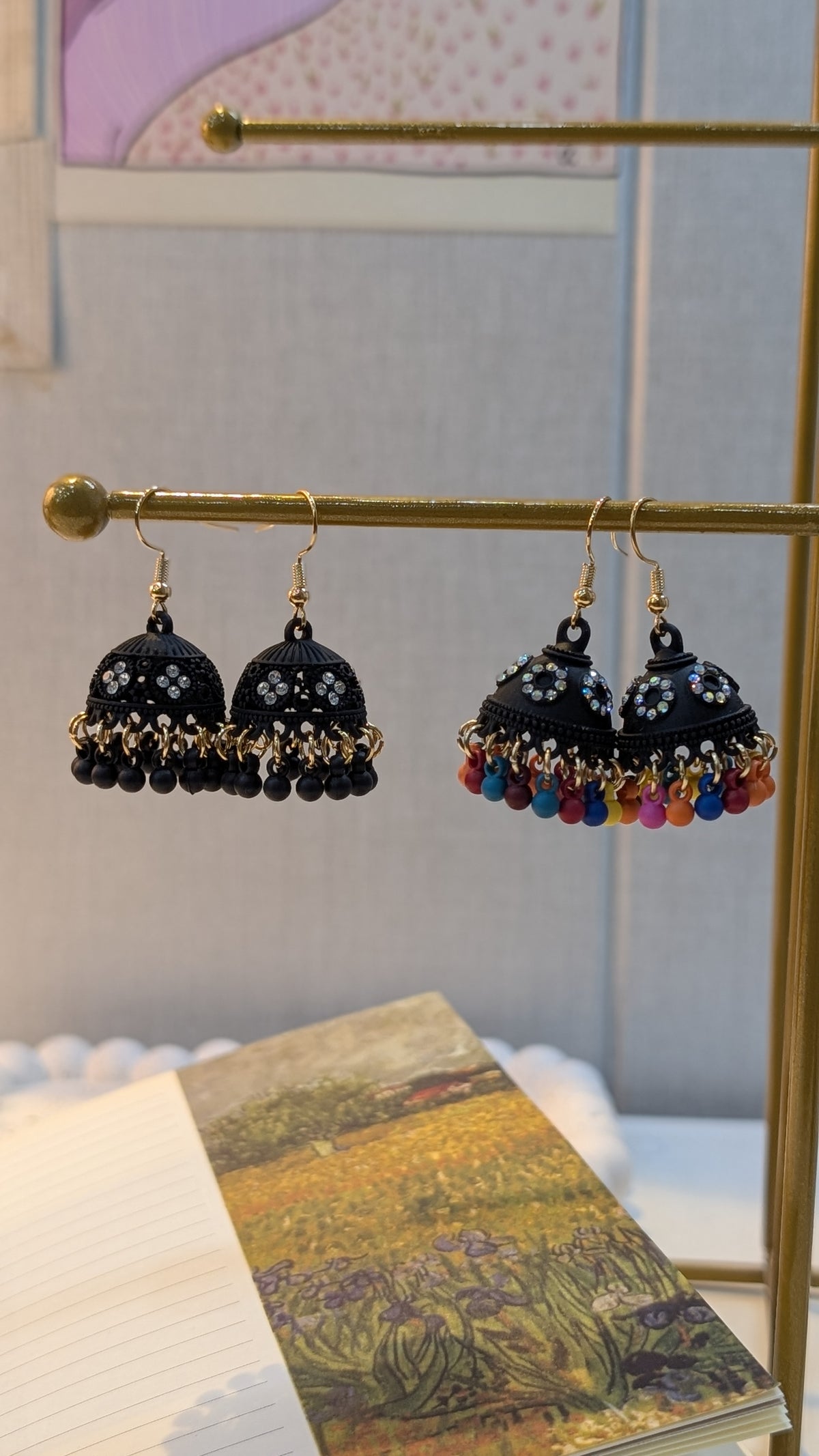 Black dome-shaped dangle earrings with small pale floral details and bead fringe, shown in dark-bead and multicolor-bead styles on a gold-tone earring stand.