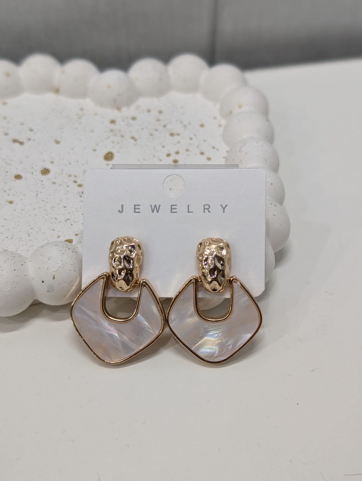 Gold-tone drop earrings with textured tops and open geometric frames around pearly iridescent white inserts.