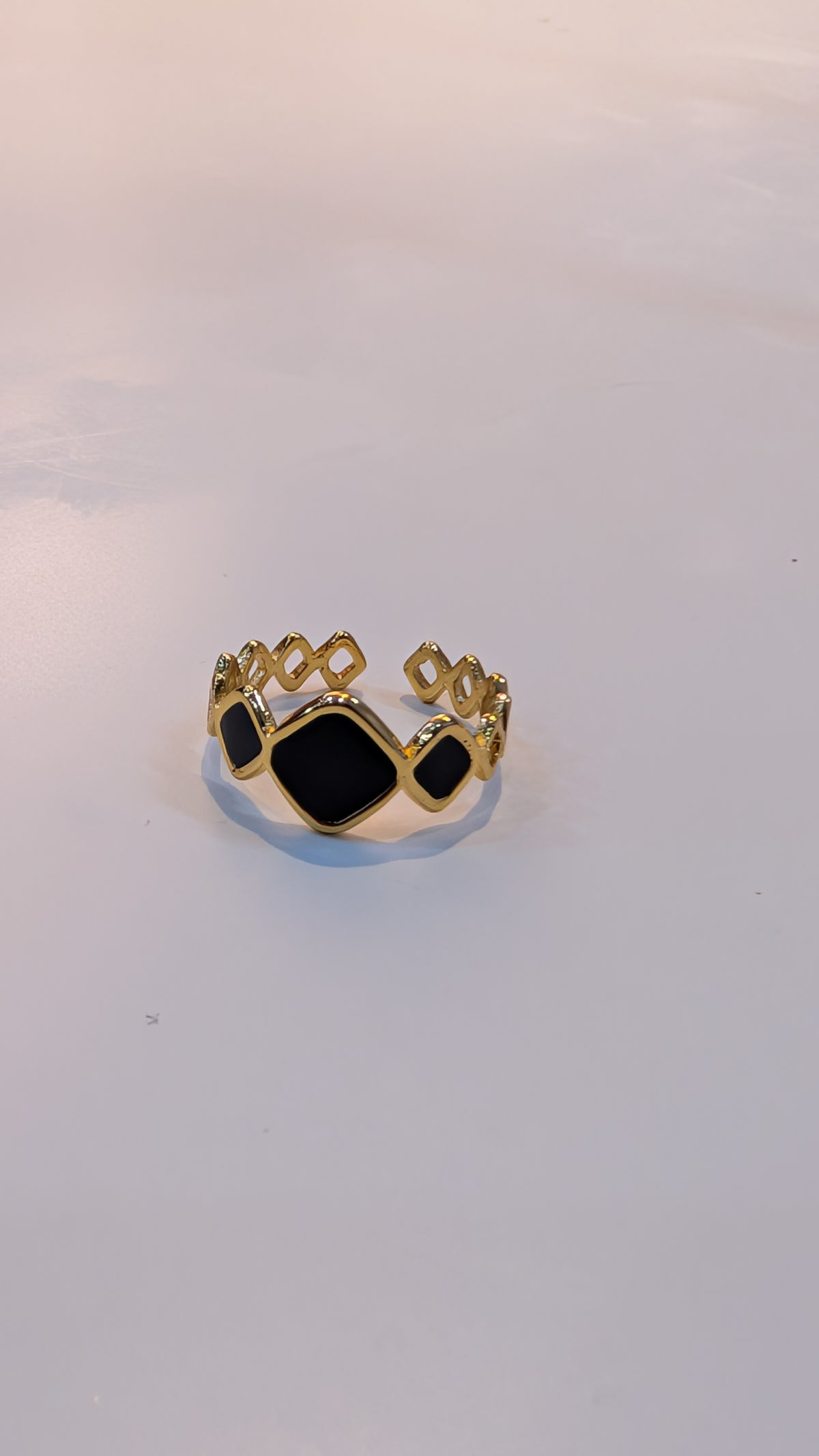 Gold-tone ring with black geometric insets and openwork shoulders on a plain light background