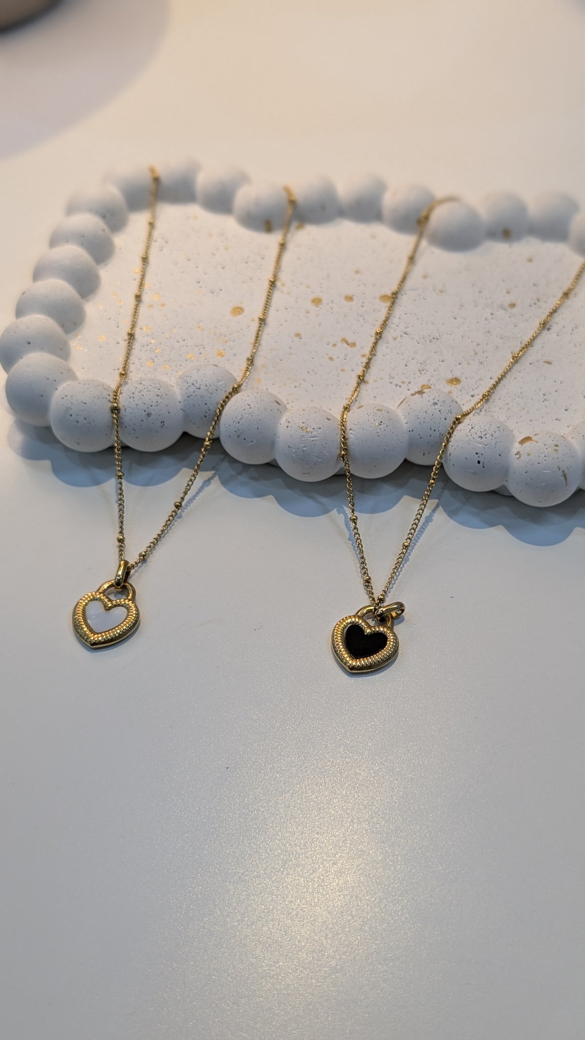 Gold-tone fine-chain necklaces with heart pendants, including an open heart outline and a black-centered heart with a textured border.