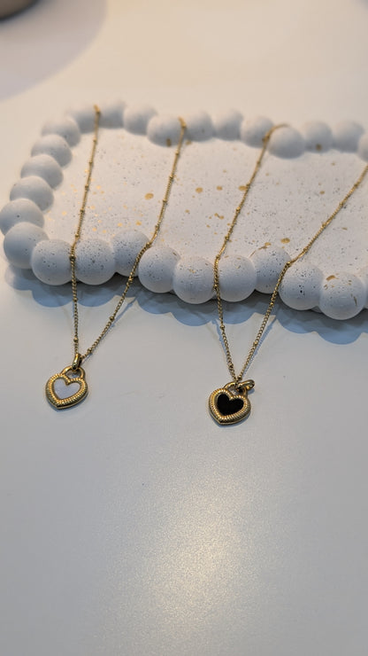 Gold-tone fine-chain necklaces with heart pendants, including an open heart outline and a black-centered heart with a textured border.