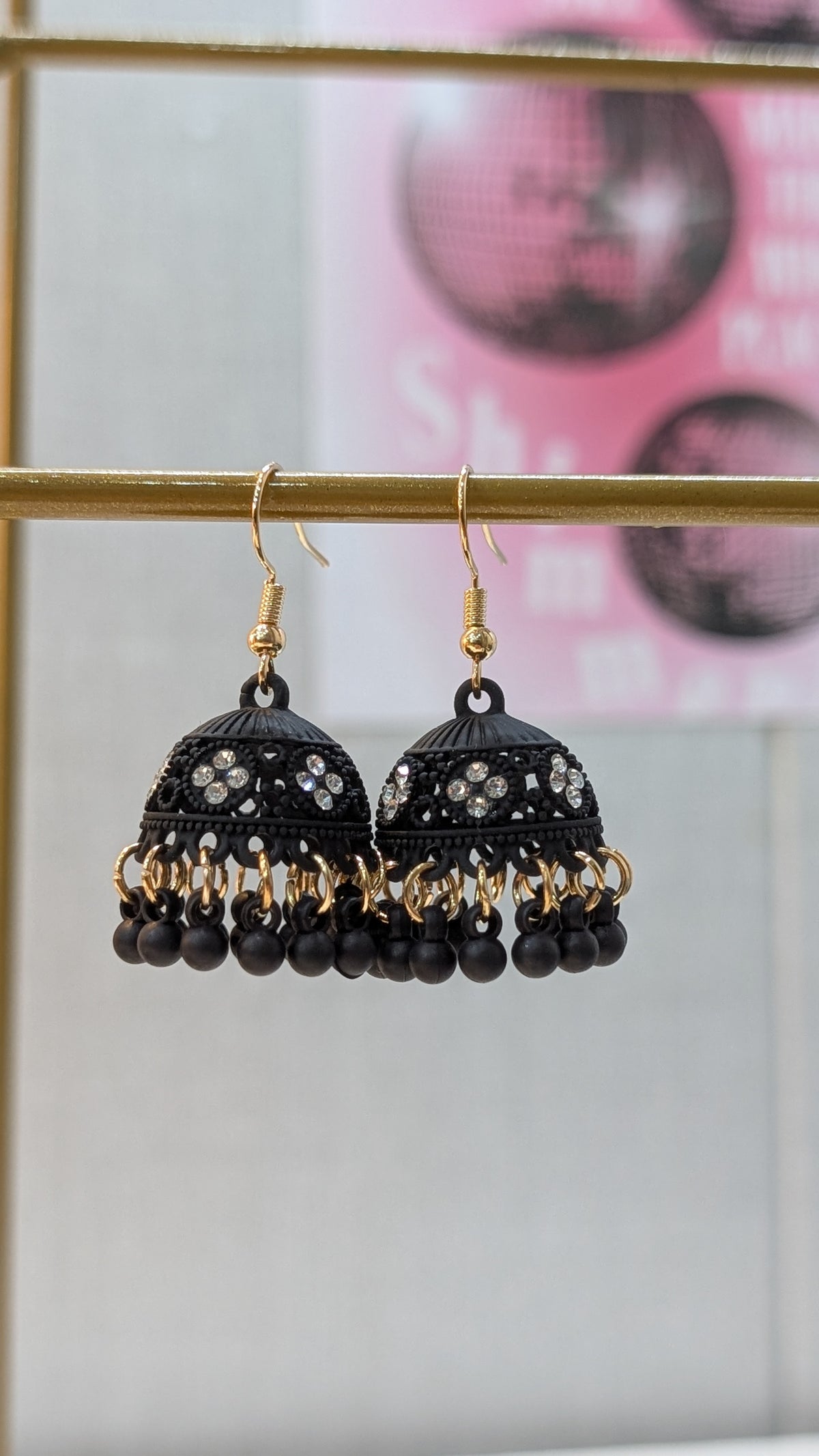 A close-up view of black dome-shaped earrings with clear accents and dangling black beads hanging from gold-tone hooks.