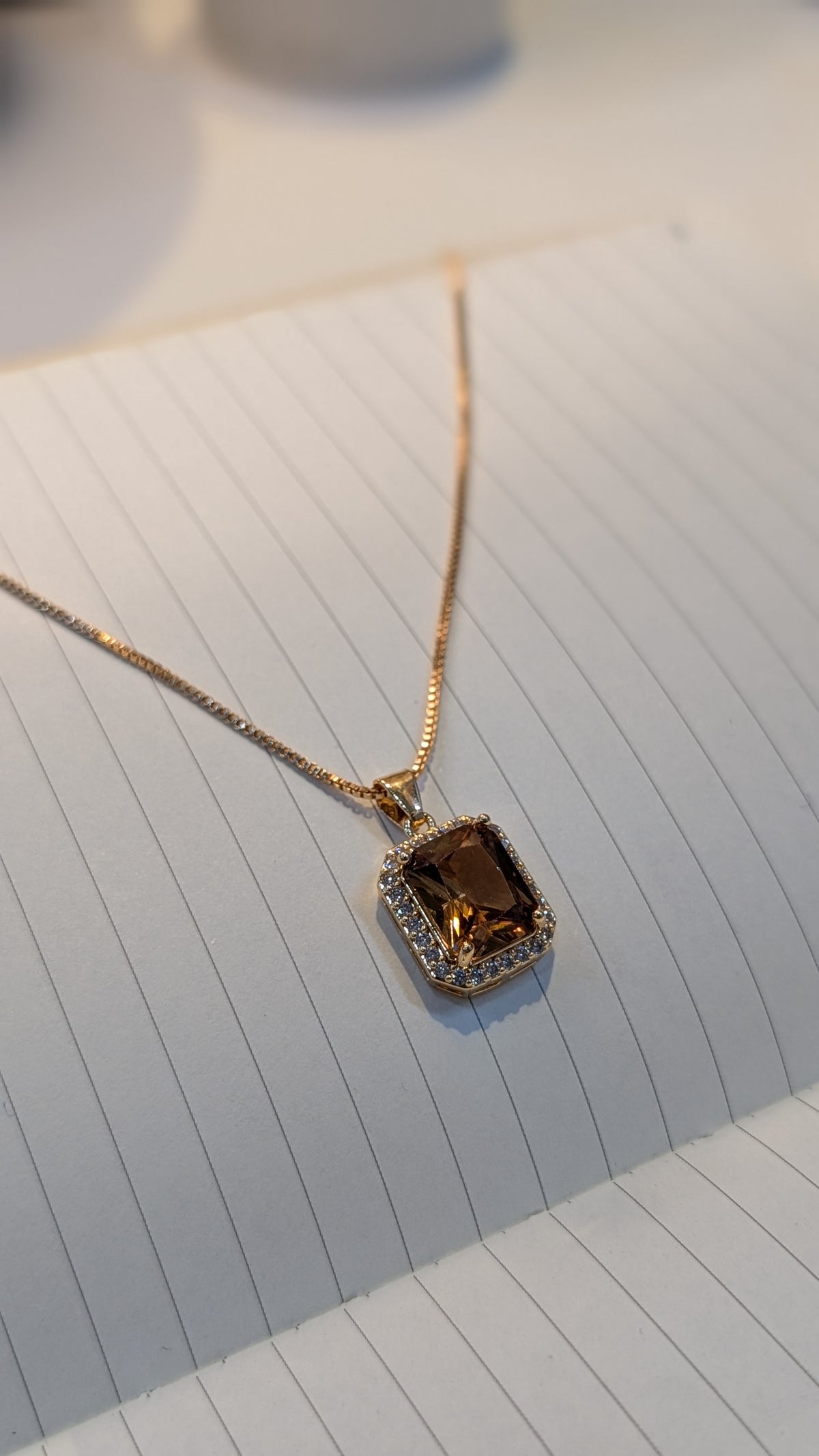 Gold-tone necklace with a thin chain and a rectangular brown faceted pendant surrounded by small clear stones.