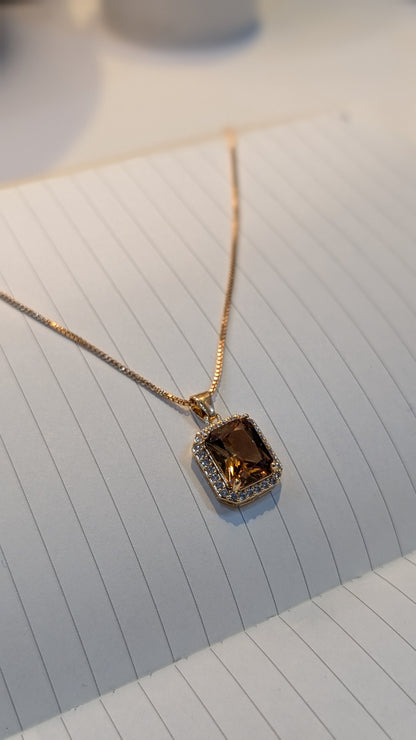 Gold-tone necklace with a thin chain and a rectangular brown faceted pendant surrounded by small clear stones.