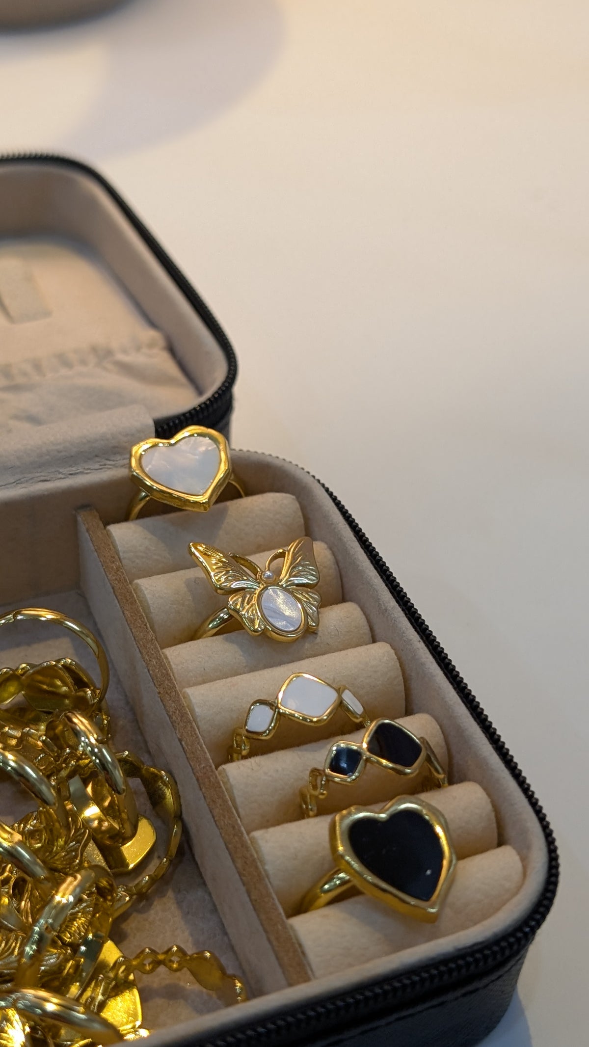Gold-tone rings with heart and butterfly shapes and black and white centers arranged in a jewelry box.