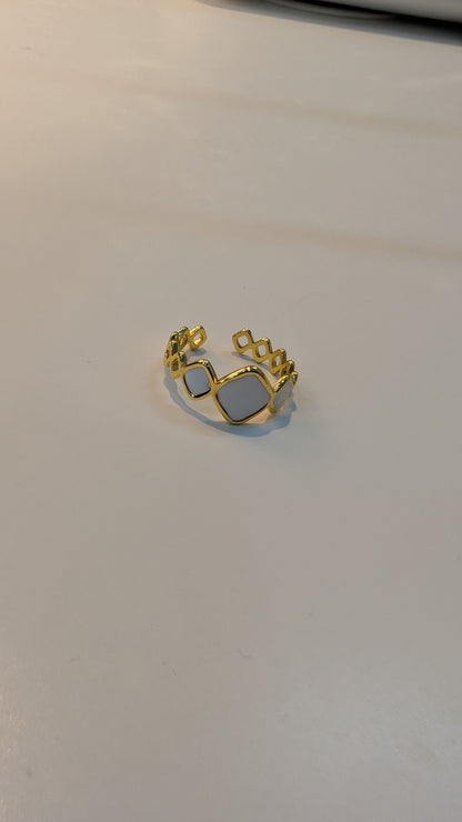 Gold-tone ring with a central rectangular cutout and small circular openings along the band.