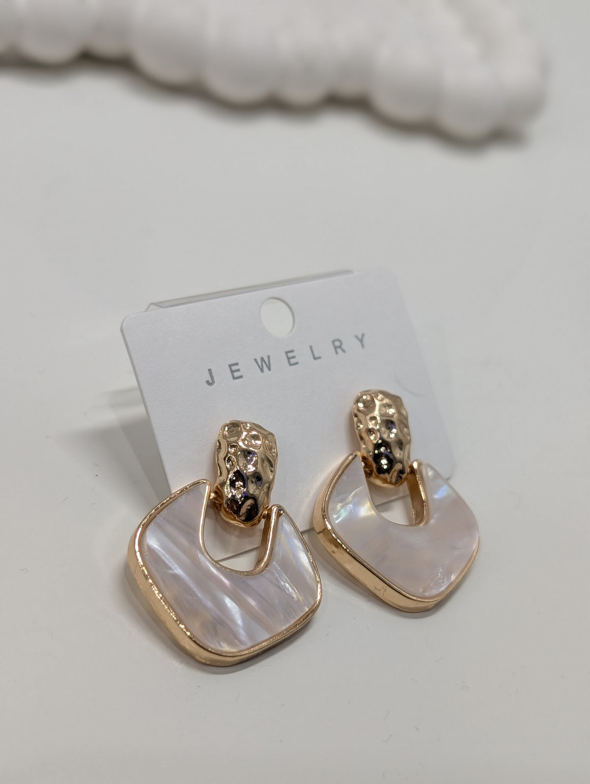 Pair of gold-tone drop earrings with textured domed tops and rounded square white iridescent insets framed in gold-tone, displayed on a white jewelry card.