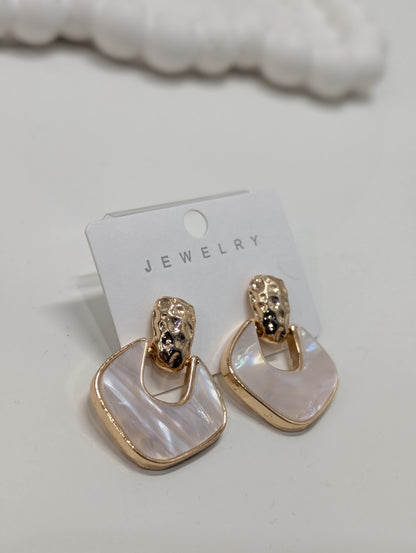 Pair of gold-tone drop earrings with textured domed tops and rounded square white iridescent insets framed in gold-tone, displayed on a white jewelry card.