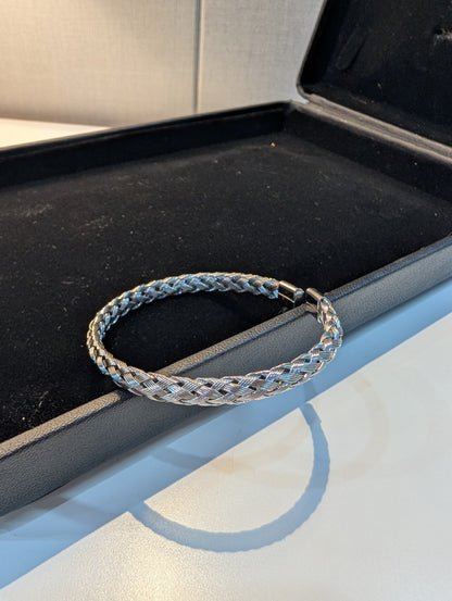 Silver-tone bangle bracelet with a braided woven pattern, displayed on a black jewellery box insert.