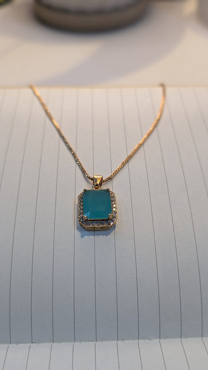 Gold-tone chain necklace with a rectangular teal pendant bordered by small clear stones.