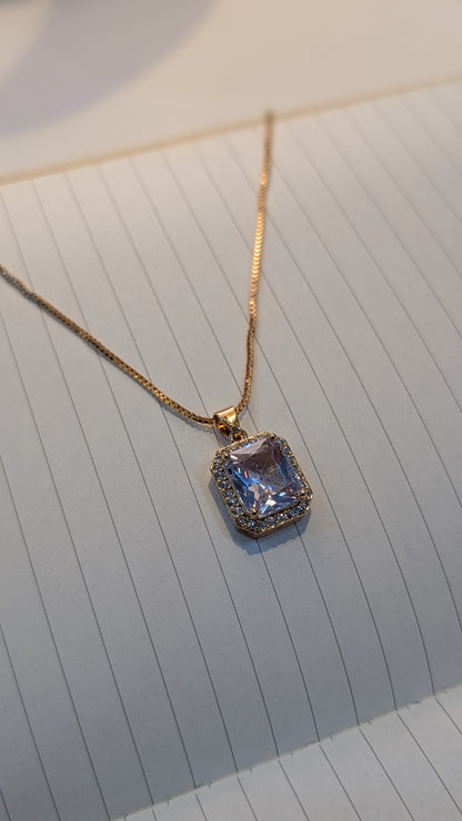 Gold-tone necklace featuring a rectangular lilac-coloured pendant surrounded by a halo of small clear stones.