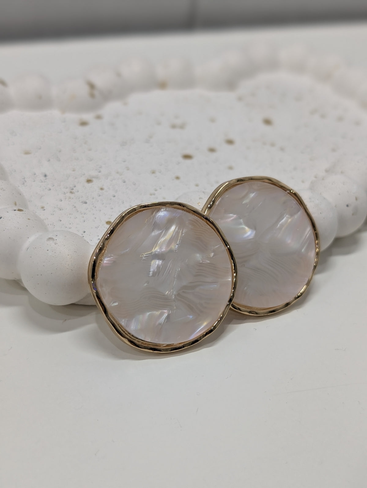 Pair of round earrings with off-white pearlescent centers and wavy gold-tone rims resting on a white tray.