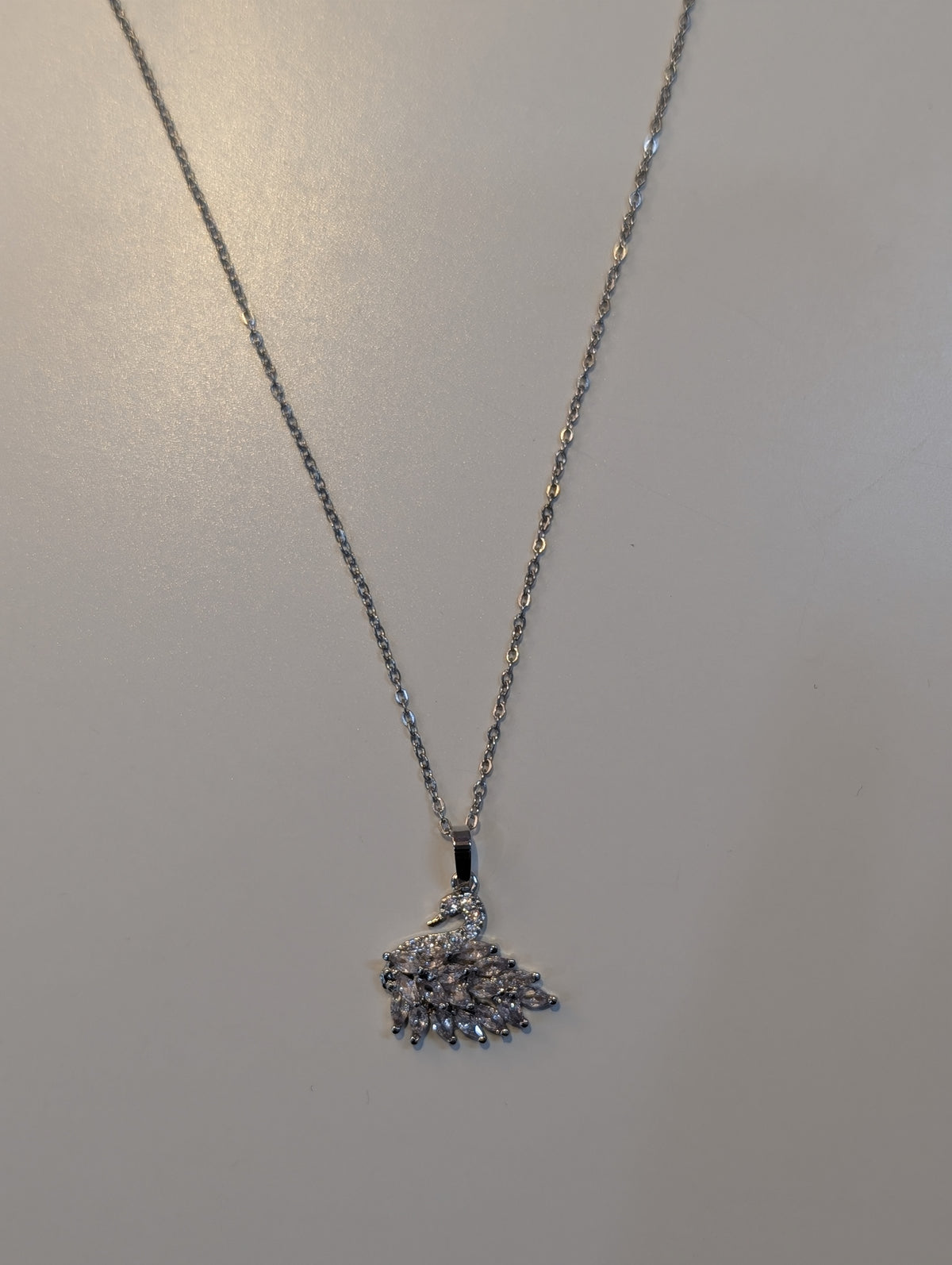 Silver-tone necklace with a fine chain and a swan pendant decorated with small clear sparkling accents and a fan-shaped tail.
