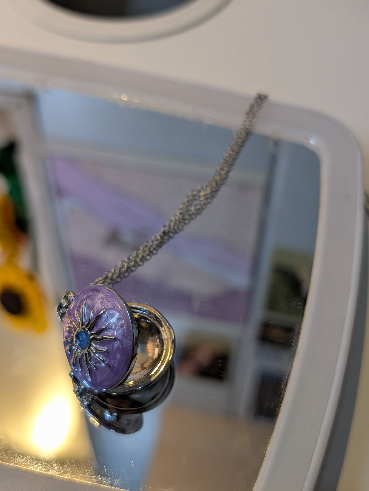 Purple domed pendant with a silver-tone sunburst motif and blue center, hanging from a silver-tone chain.