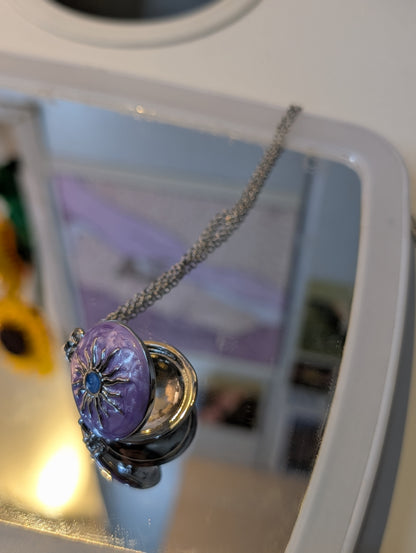 Purple domed pendant with a silver-tone sunburst motif and blue center, hanging from a silver-tone chain.